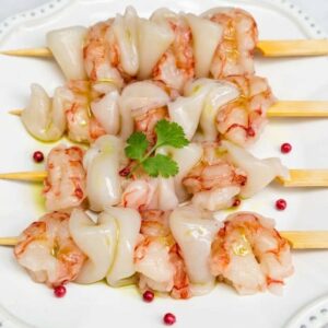 shrimp and cuttlefish brochette cooked on a plate with sauce and seasoning